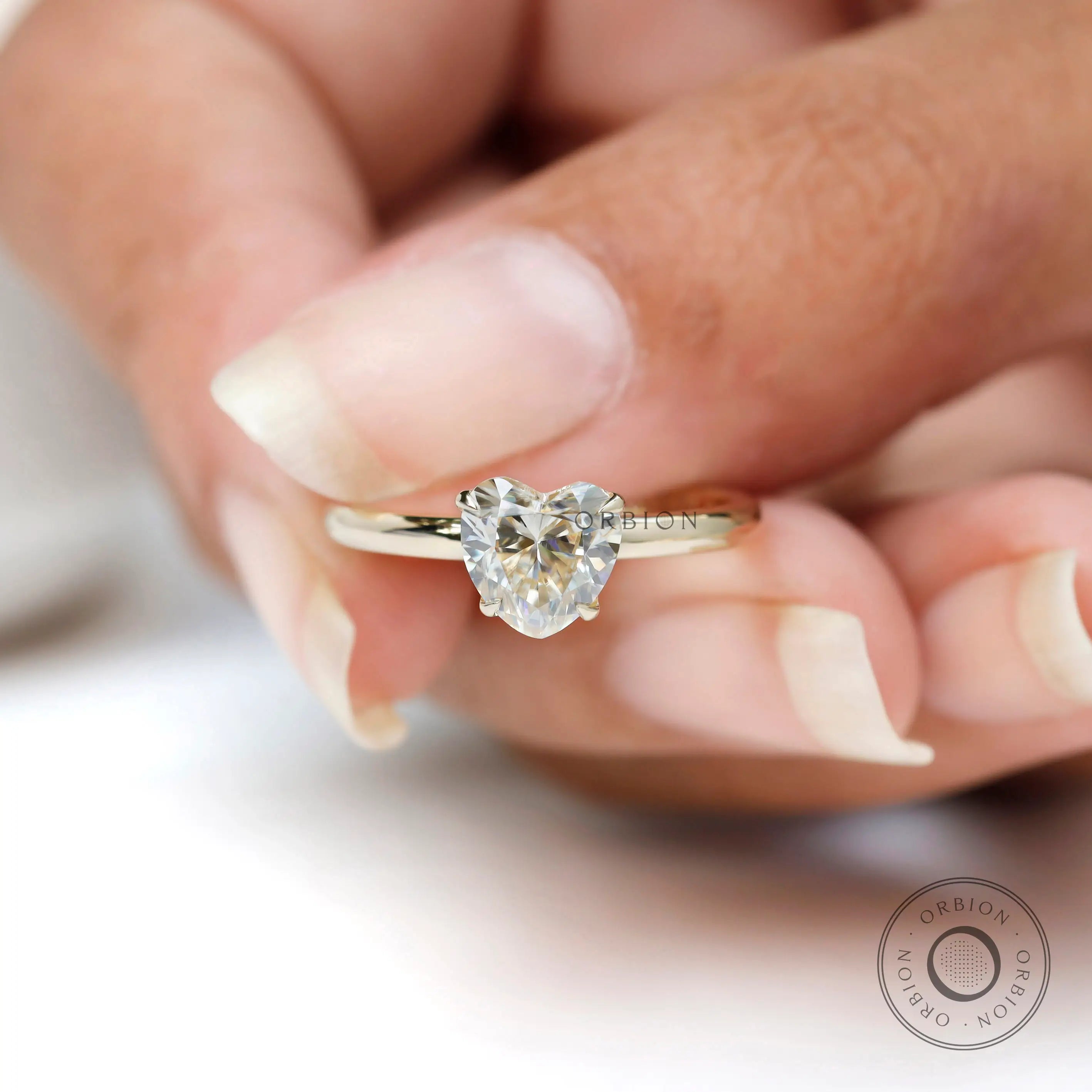 Close up side angle heart solitaire ring held against soft white background