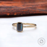 Modern bezel solitaire ring with dark emerald cut moissanite.