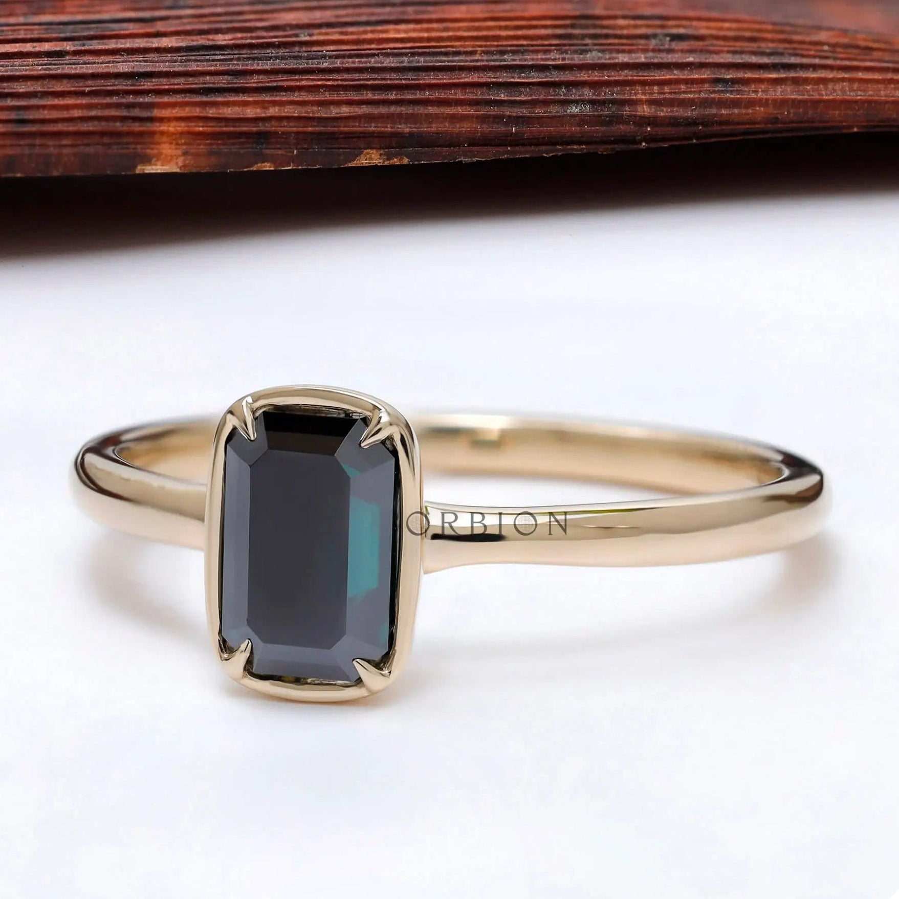 Modern bezel solitaire ring with dark emerald cut moissanite.