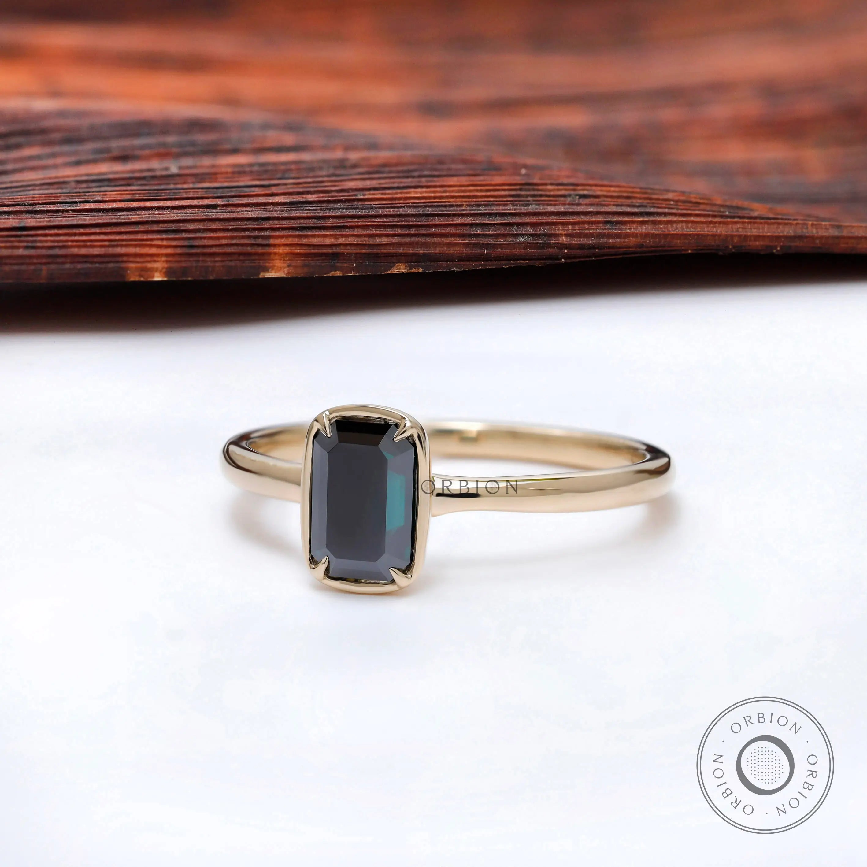 Modern bezel solitaire ring with dark emerald cut moissanite.