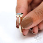 Bezel set emerald cut moissanite ring held between fingers.