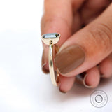 Bezel set emerald cut moissanite ring held between fingers.