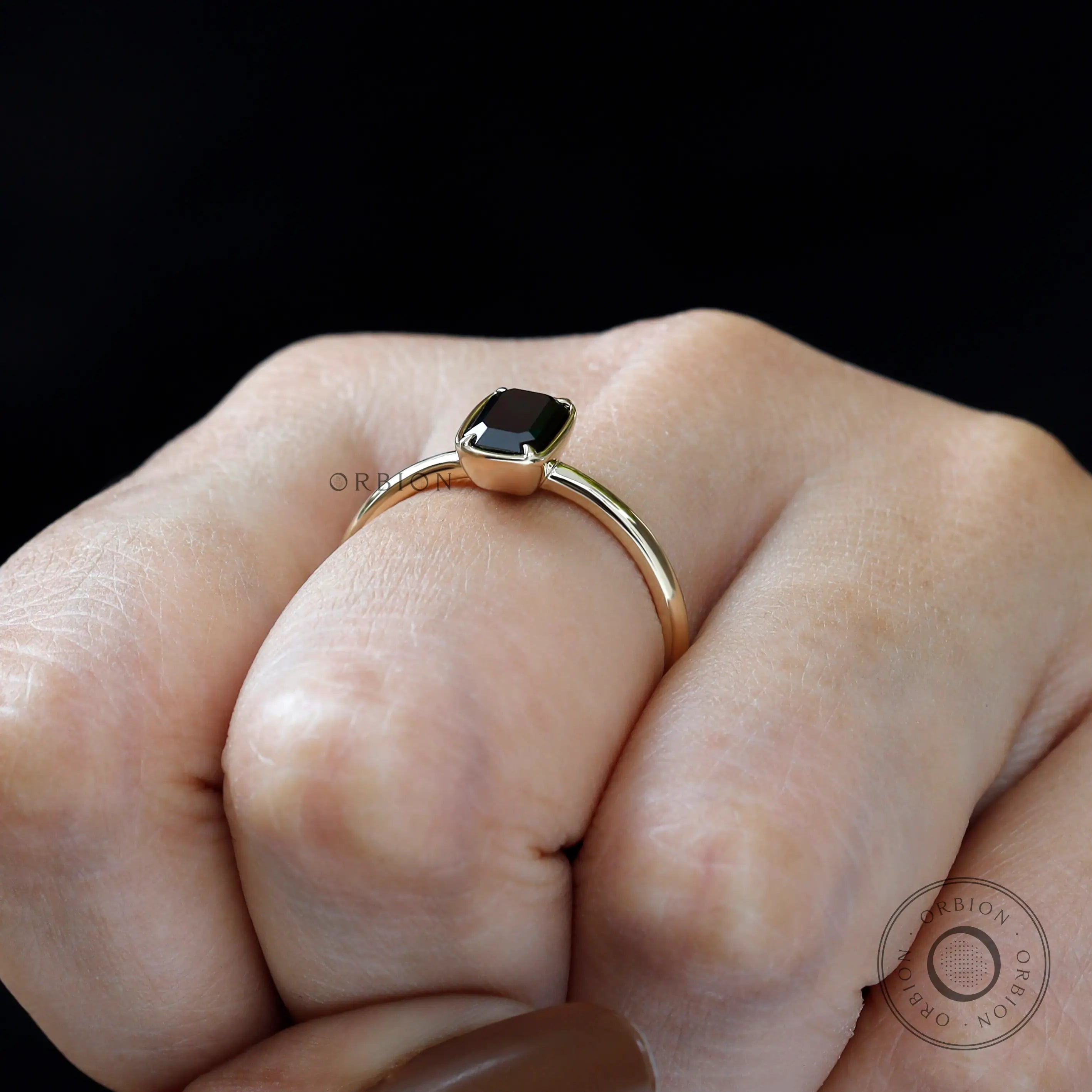 Bezel set emerald cut black green moissanite ring worn on hand.