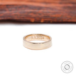 Inside view of wide gold wedding band showing date engraving and gold hallmark.