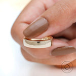 Close-up side view of thick yellow gold wedding band held between fingers.