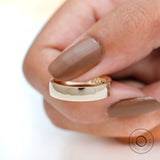 Close-up side view of thick yellow gold wedding band held between fingers.
