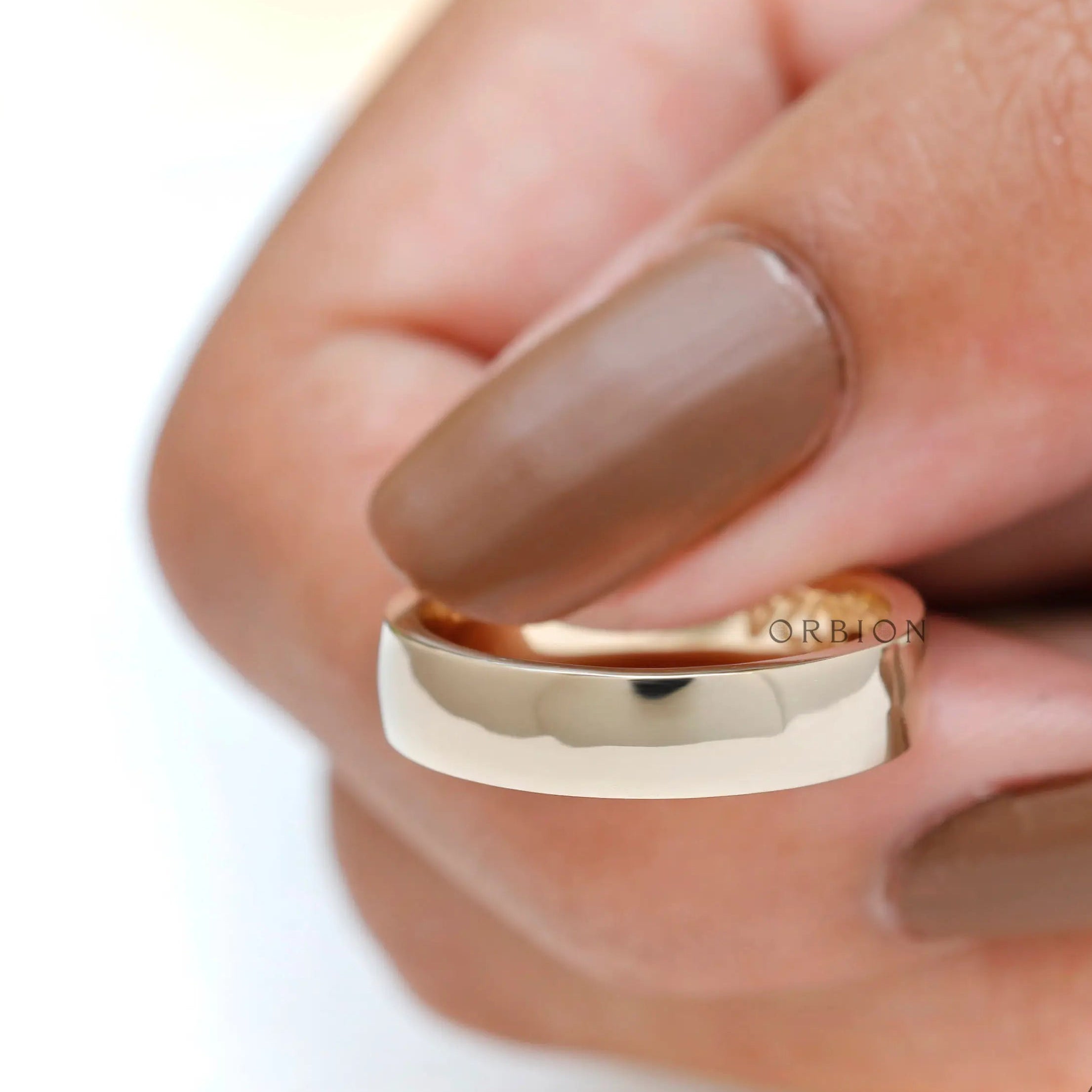 Close-up side view of thick yellow gold wedding band held between fingers.