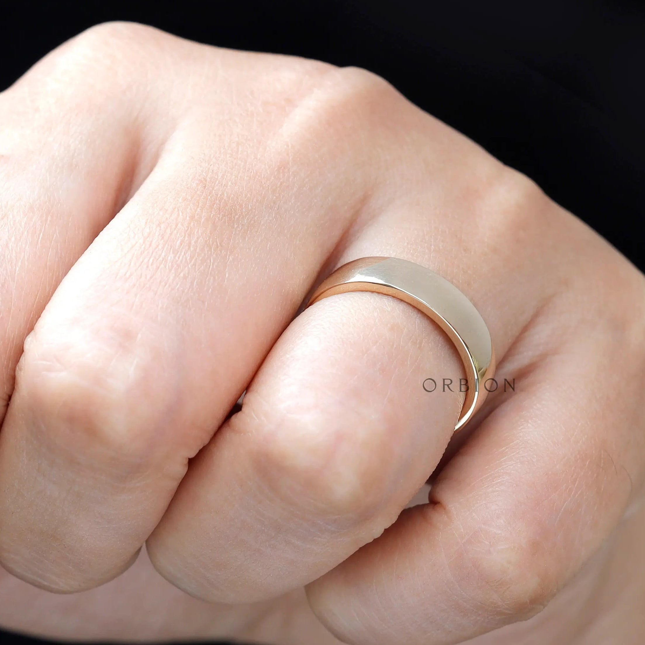 Close-up of yellow gold comfort fit wedding band on finger showing high polish shine.