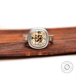 Dark champagne OMC cushion moissanite bezel ring, front view on wood