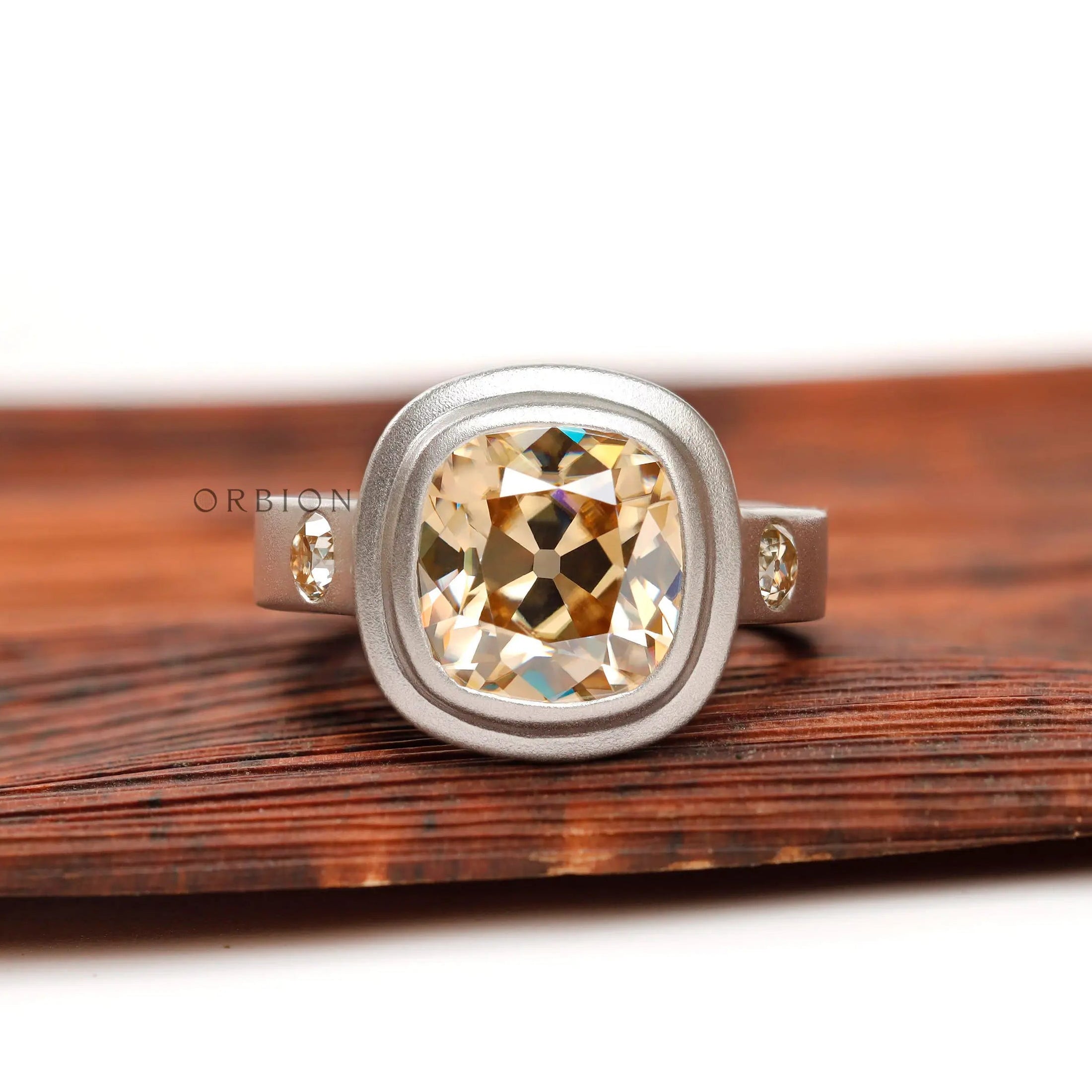 Dark champagne OMC cushion moissanite bezel ring, front view on wood
