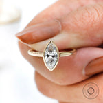 On-hand close-up of marquise bezel solitaire ring in yellow gold