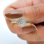 Hand-held closeup of round lab diamond with floral cluster halo details.