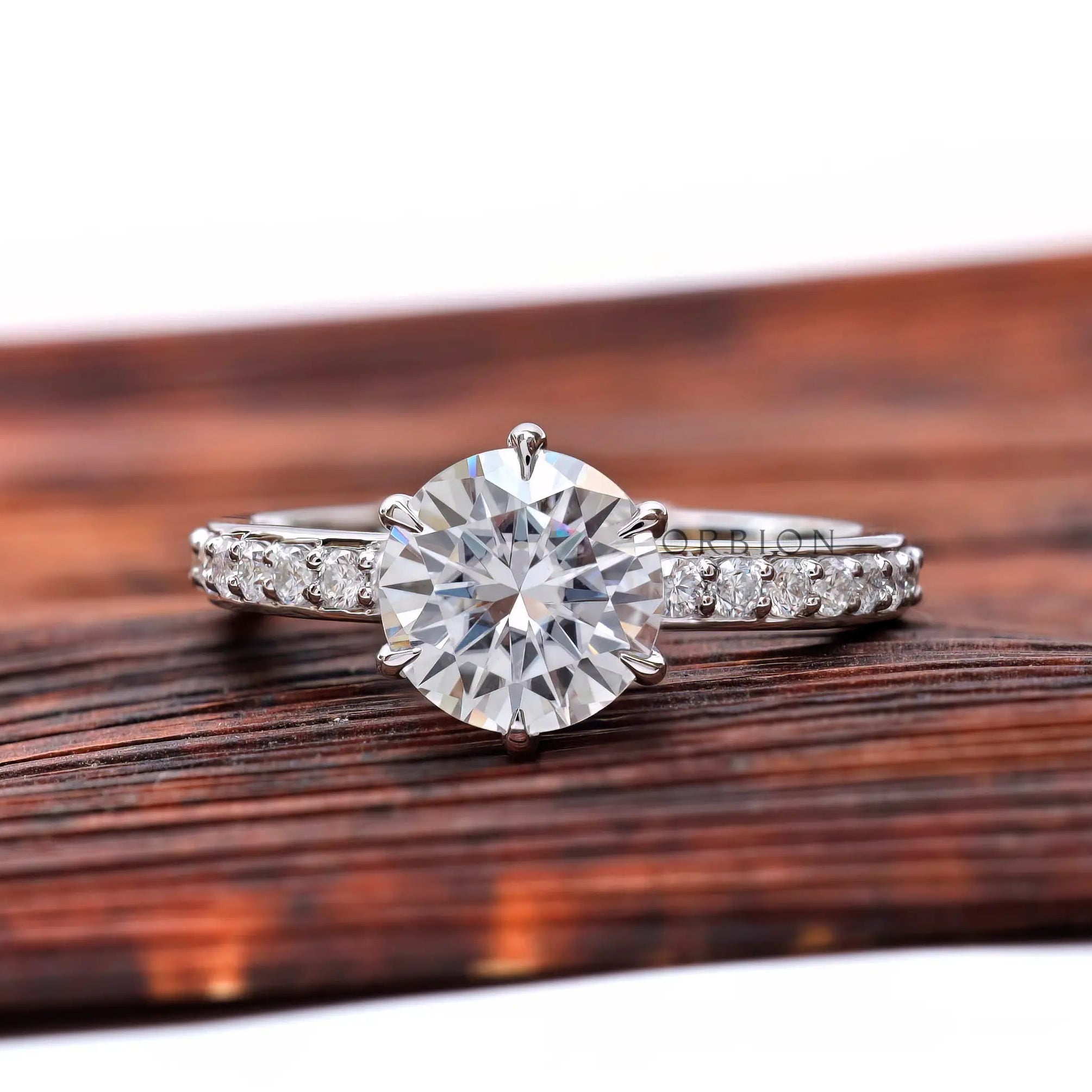 Round moissanite solitaire engagement ring with pave band, front view.