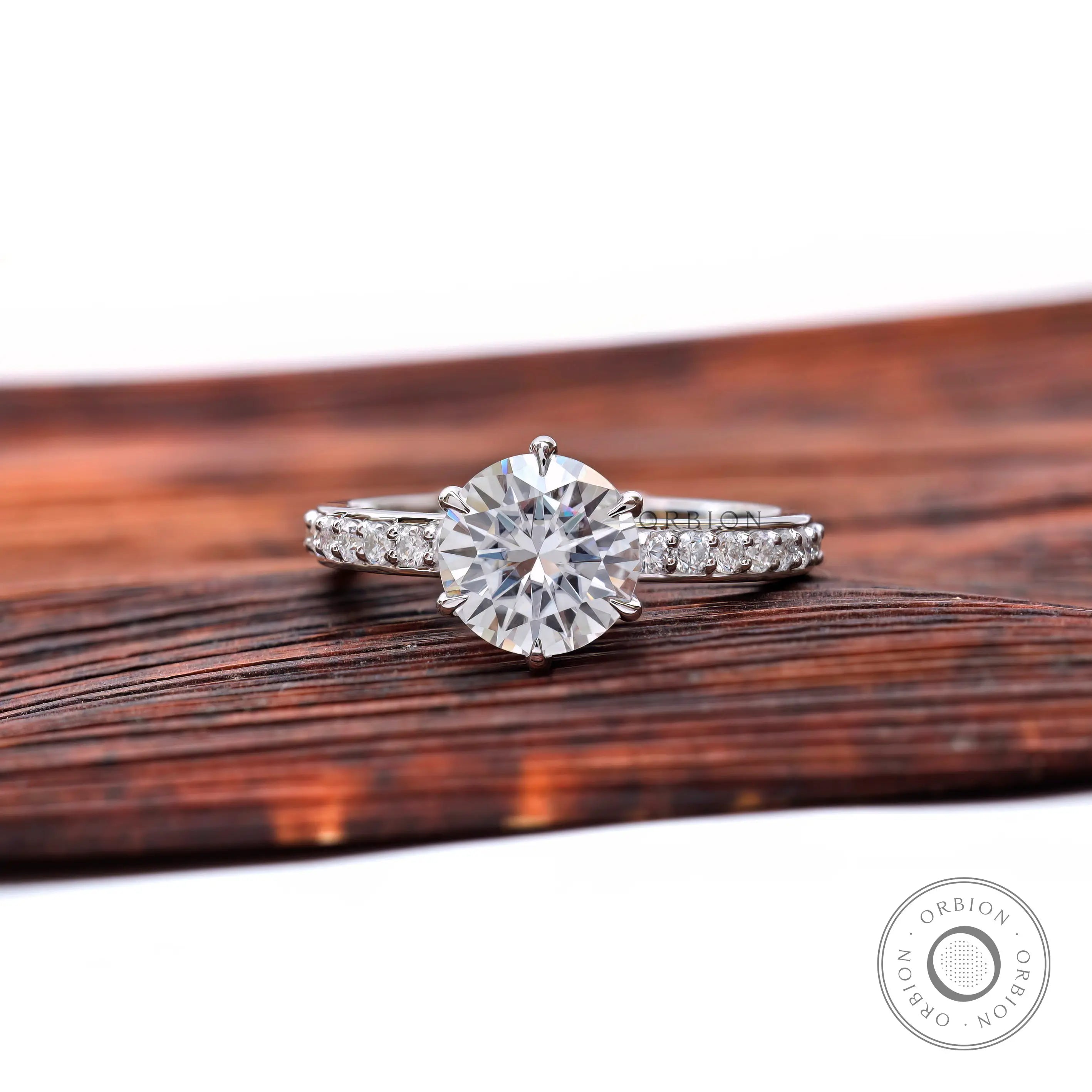 Round moissanite solitaire engagement ring with pave band, front view.