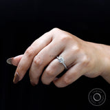 Round moissanite solitaire engagement ring worn on hand against black background.