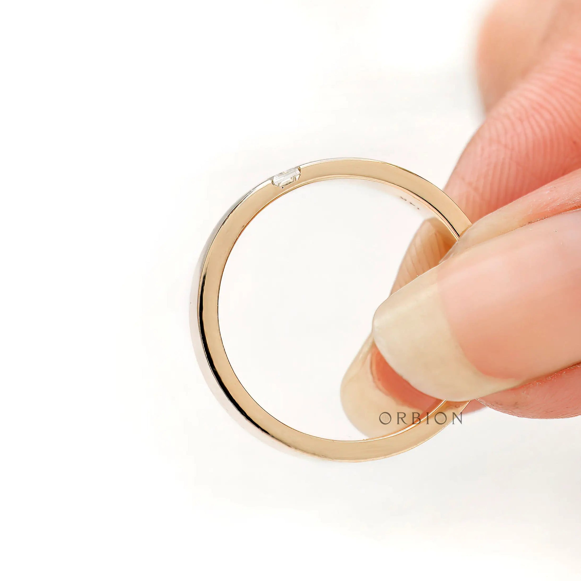 Edge detail of comfort fit band with flush set baguette, shown while held.