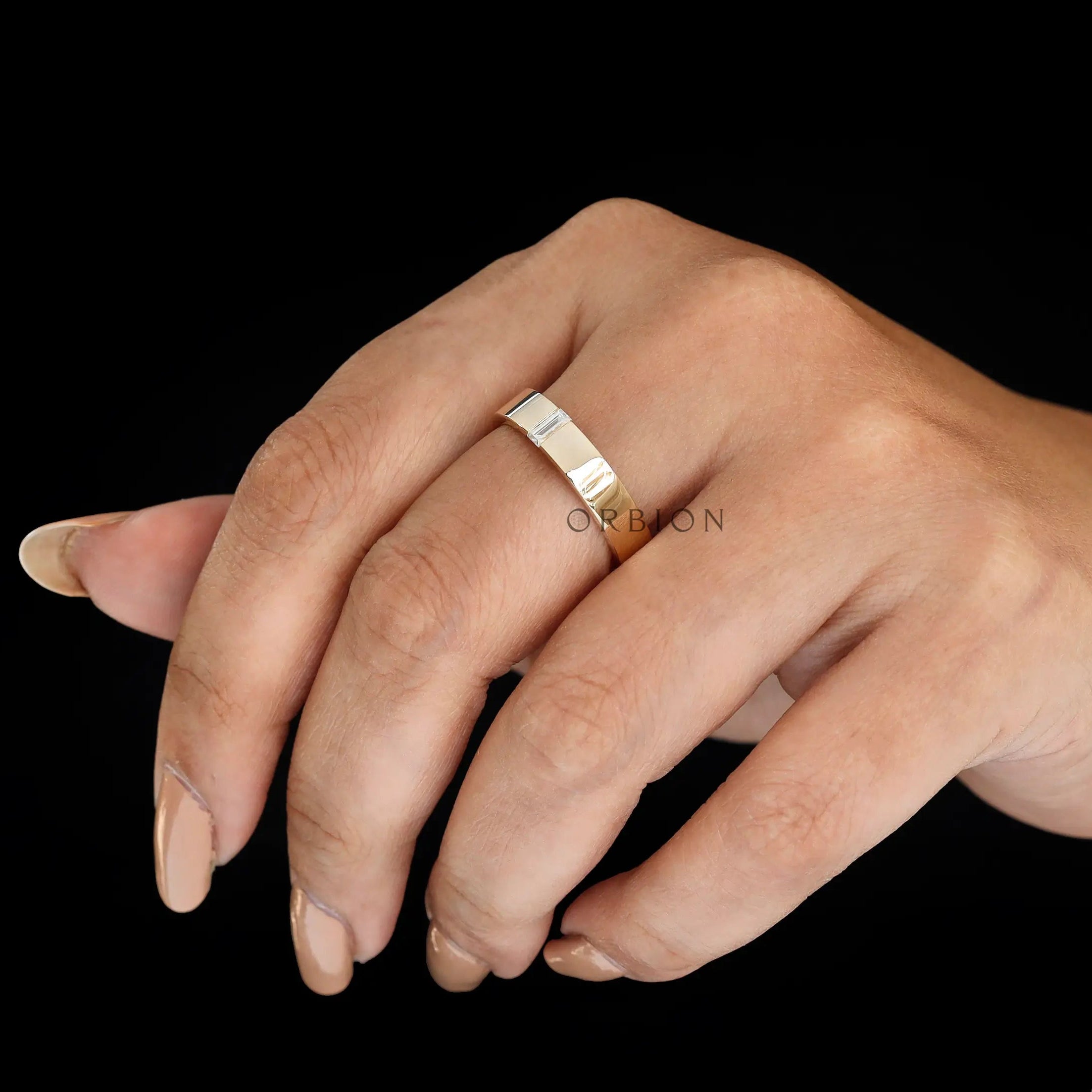 Lifestyle image of minimalist comfort fit wedding band with baguette moissanite worn on hand.