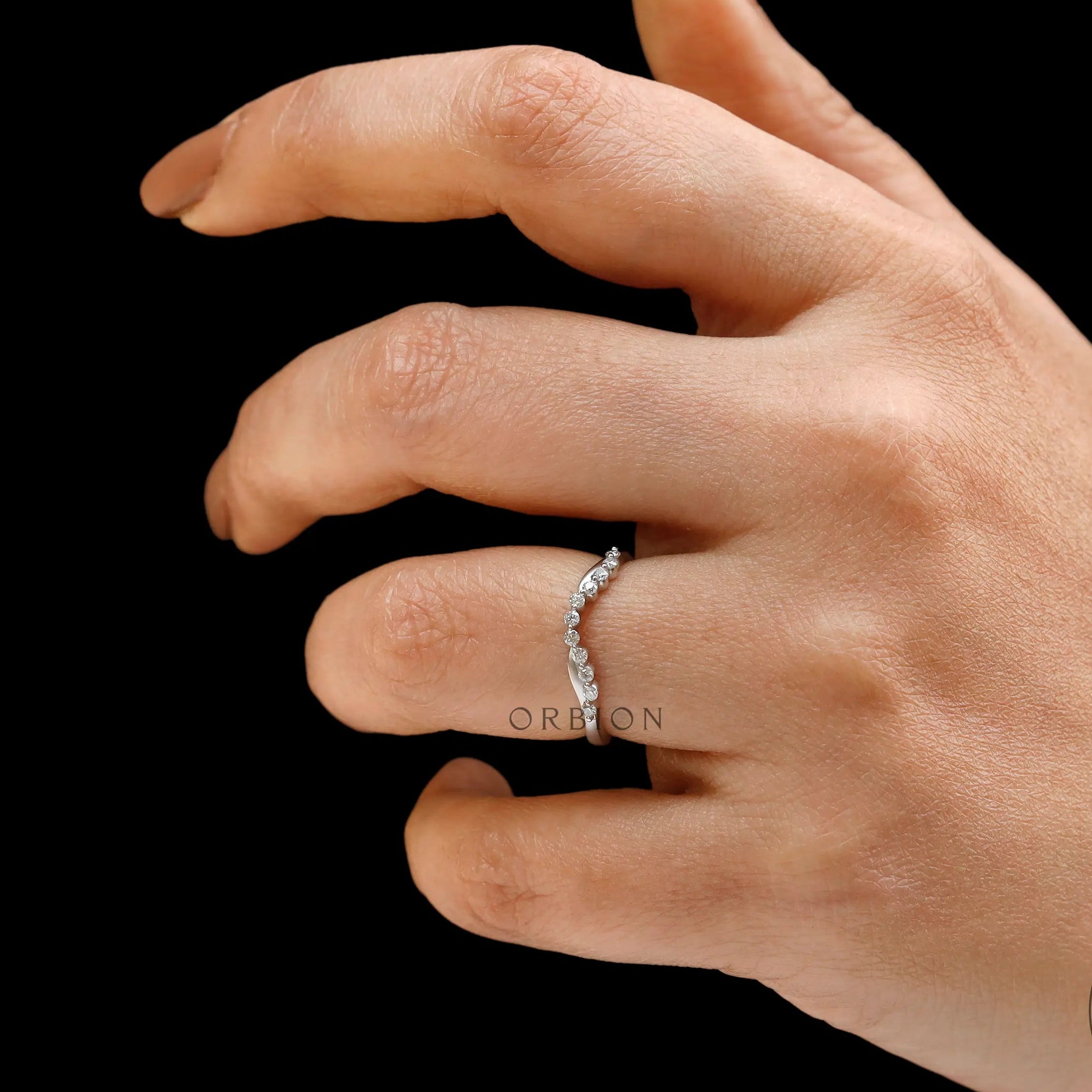 Hand wearing curved bubble prong wedding band on black background