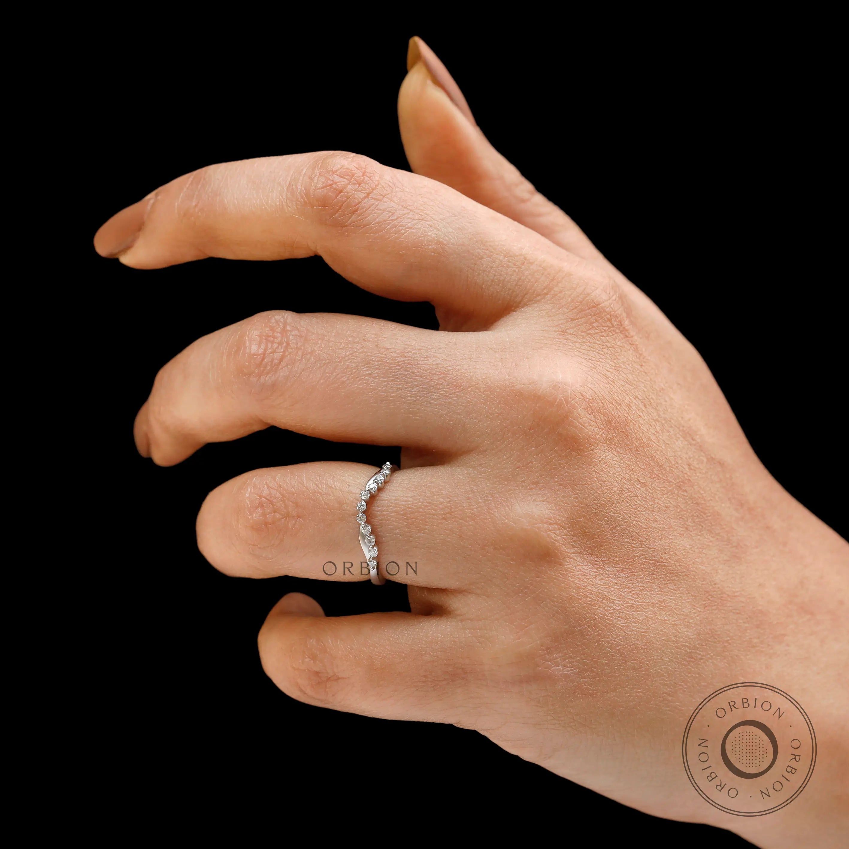 Hand wearing curved bubble prong wedding band on black background