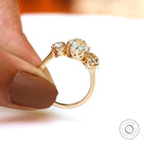 Side profile three-stone ring held between fingers with open gallery.