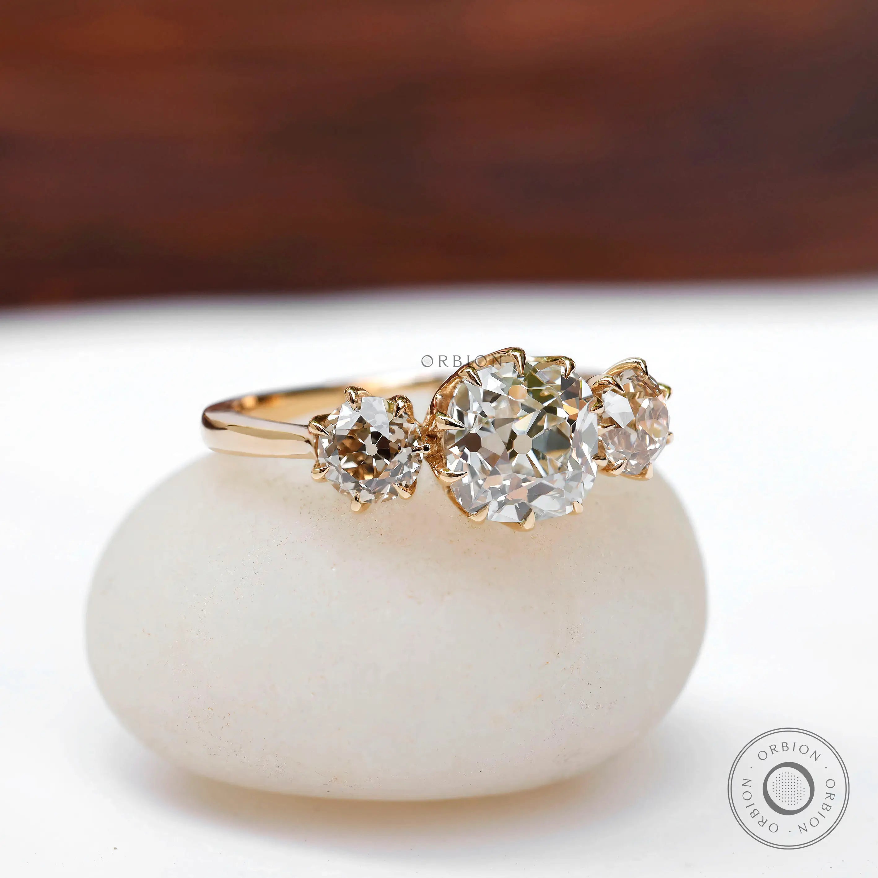 Angled front view three-stone ring on pebble backdrop.