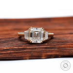 Front view of Asscher moissanite three stone ring in yellow gold on wooden surface