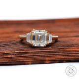 Front view of Asscher moissanite three stone ring in yellow gold on wooden surface
