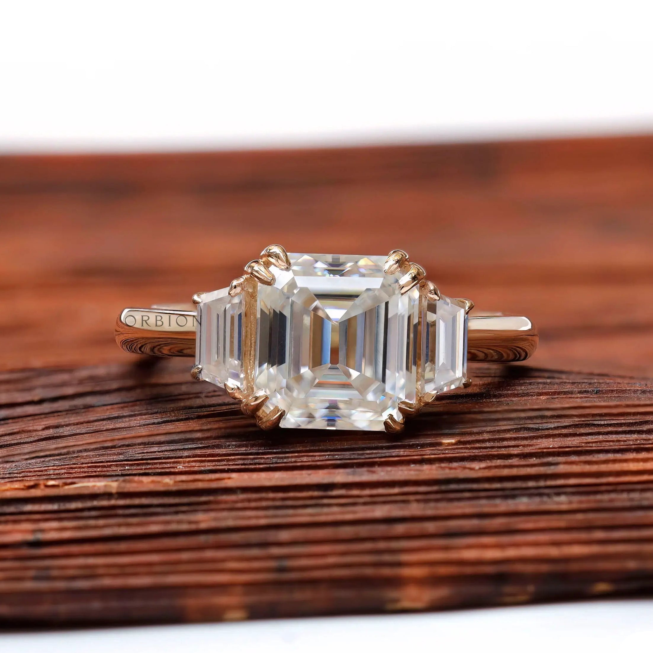 Front view of Asscher moissanite three stone ring in yellow gold on wooden surface