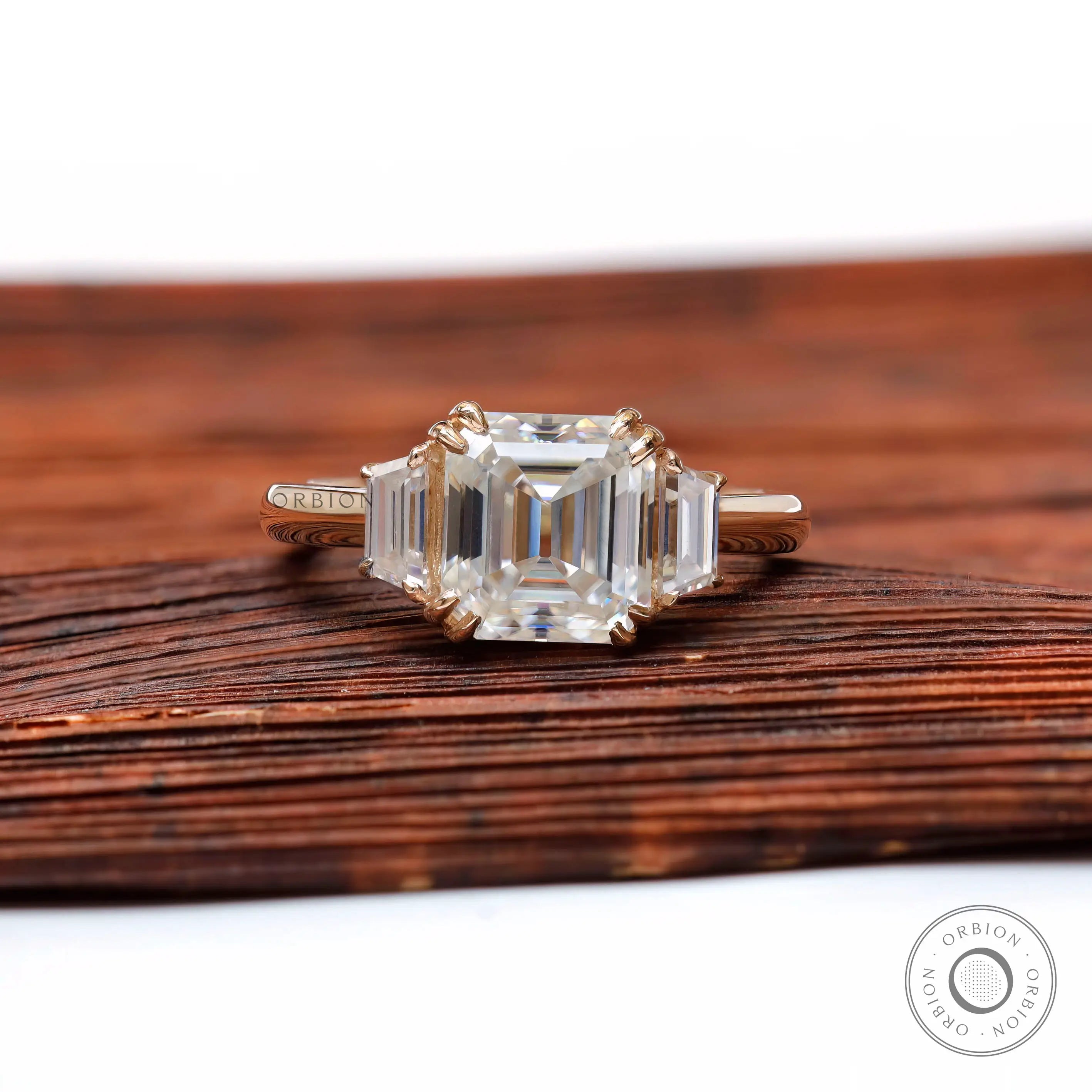 Front view of Asscher moissanite three stone ring in yellow gold on wooden surface