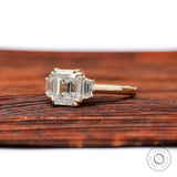 Angled front view showing step cut Asscher center and tapered side stones on wood