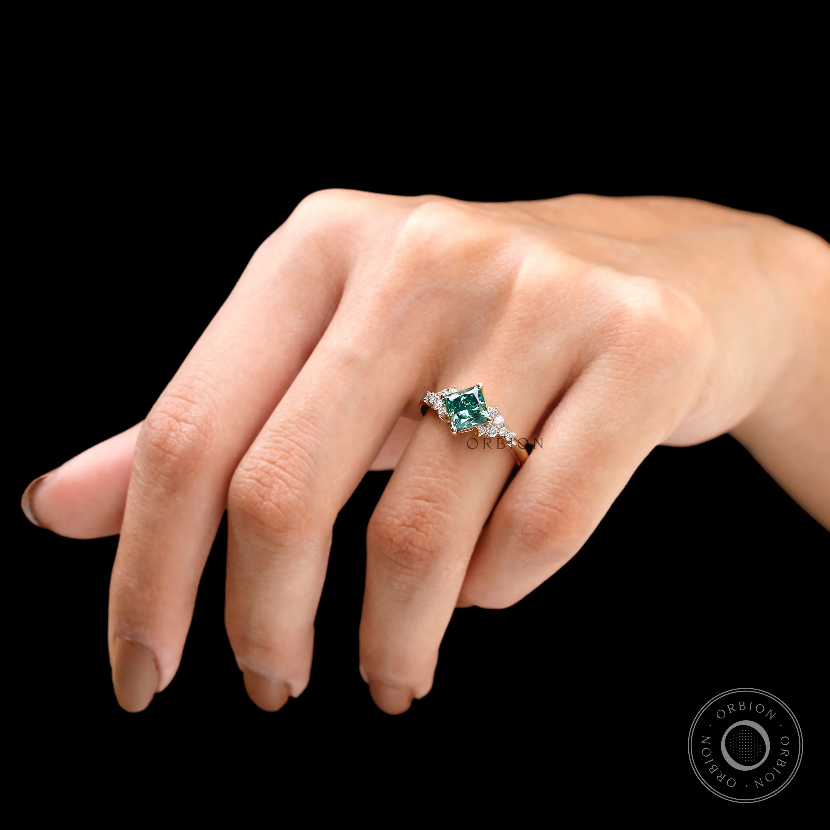 Hand model displaying the green moissanite engagement ring with diamonds.