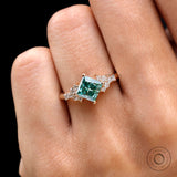 Close-up of princess-cut green moissanite ring worn on hand.
