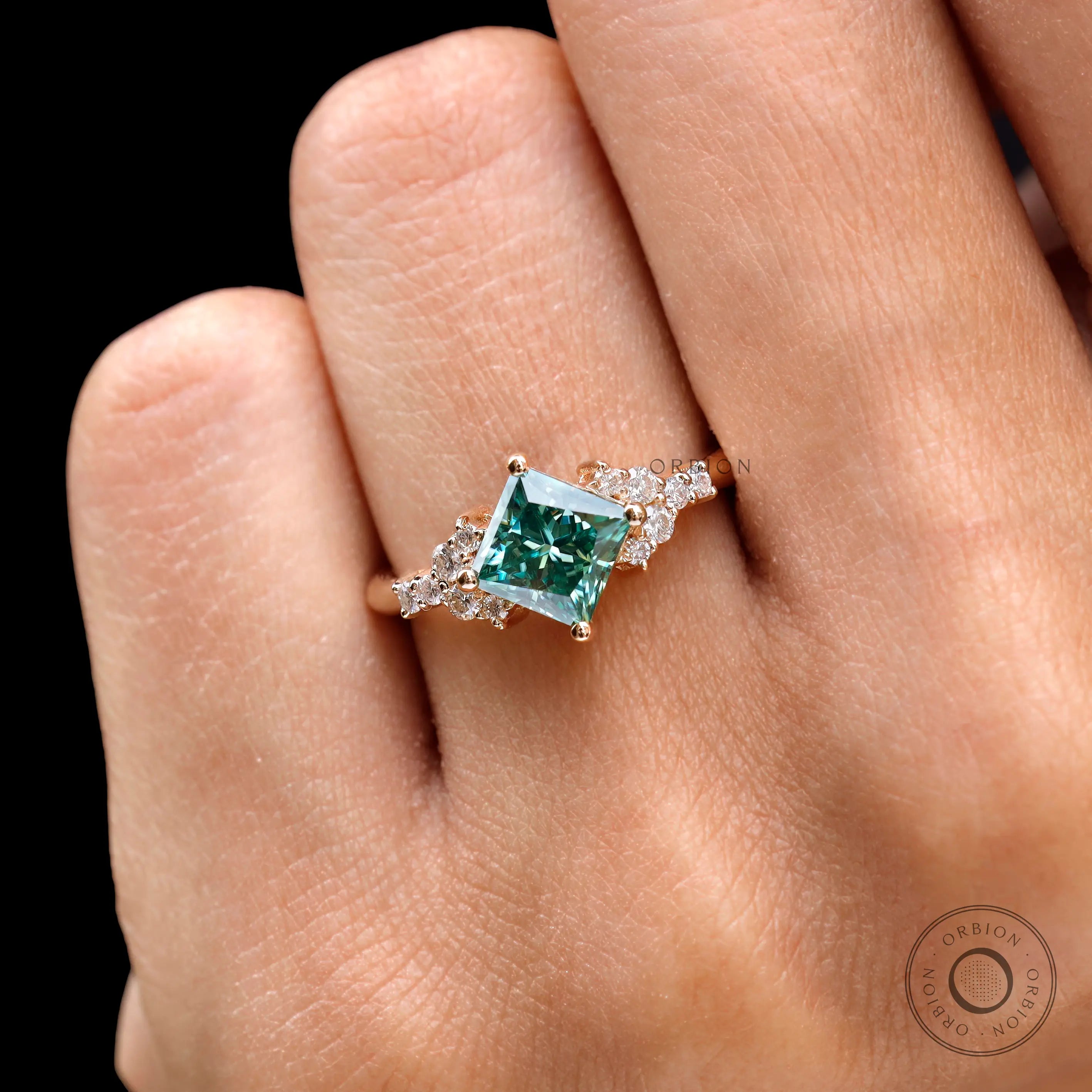 Close-up of princess-cut green moissanite ring worn on hand.
