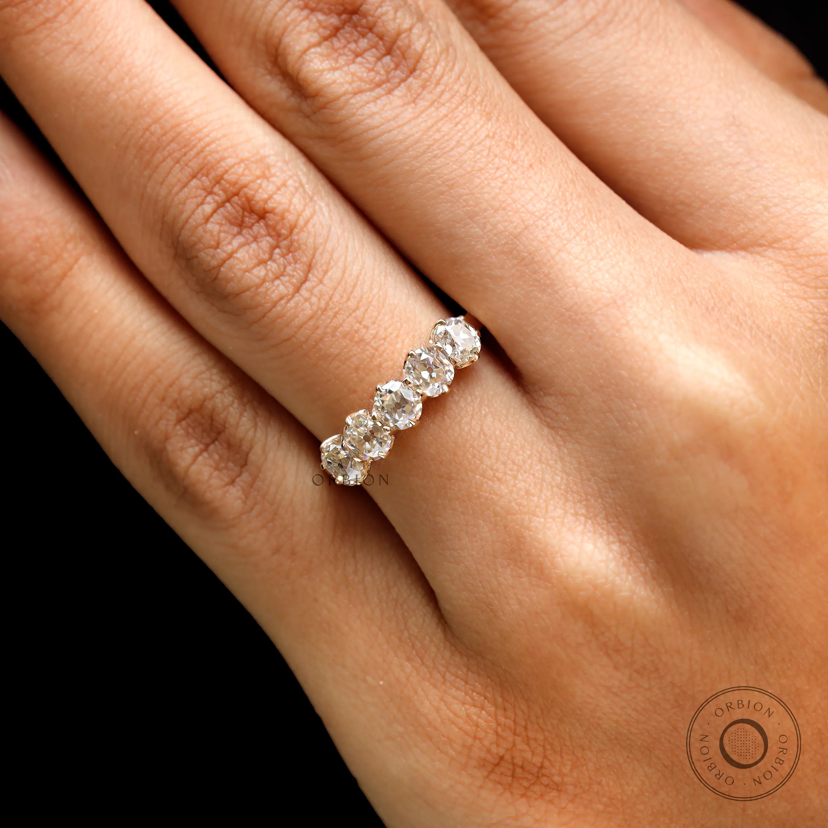 Lifestyle on-hand photo of five stone moissanite wedding band in yellow gold