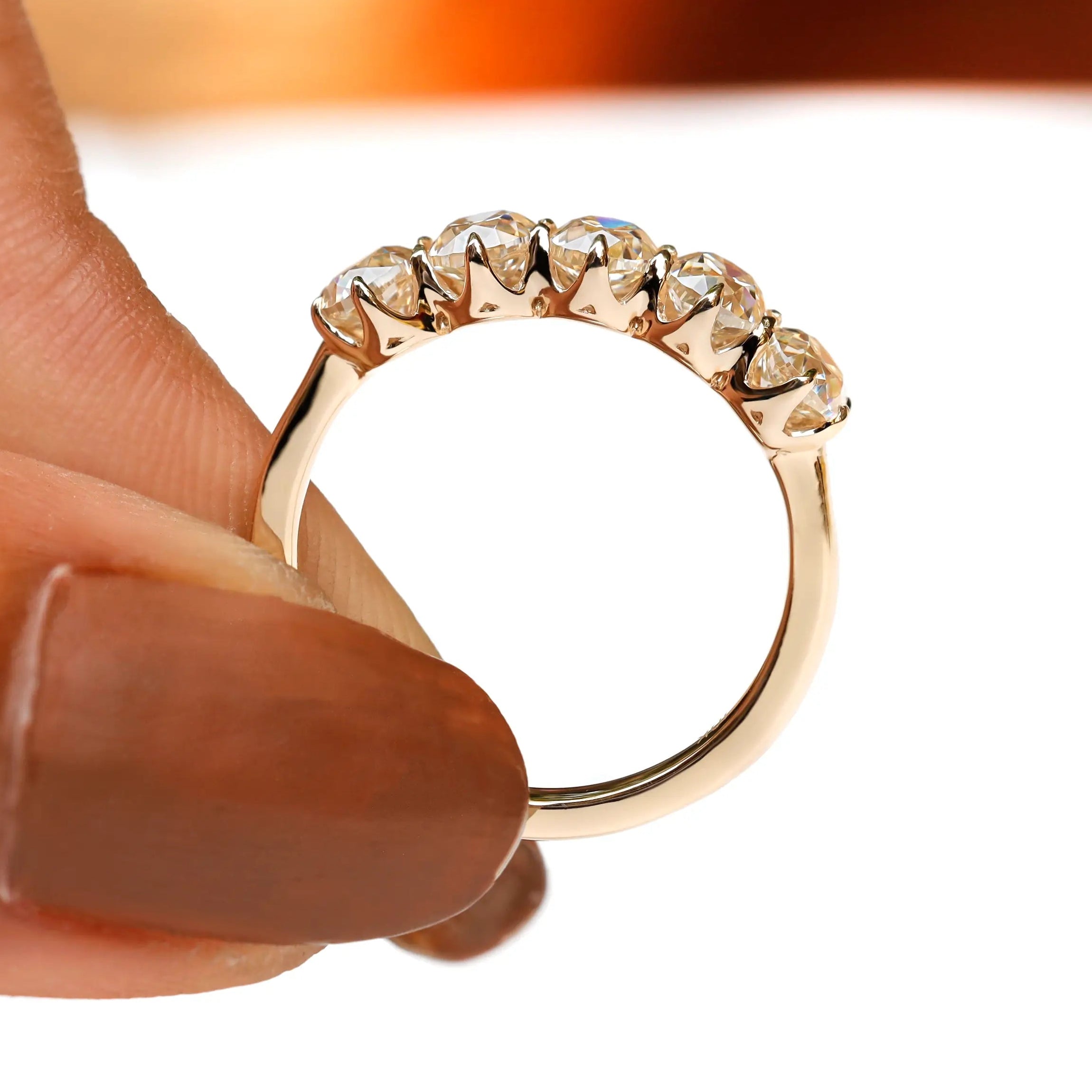 Profile close-up of five stone moissanite band held between fingers