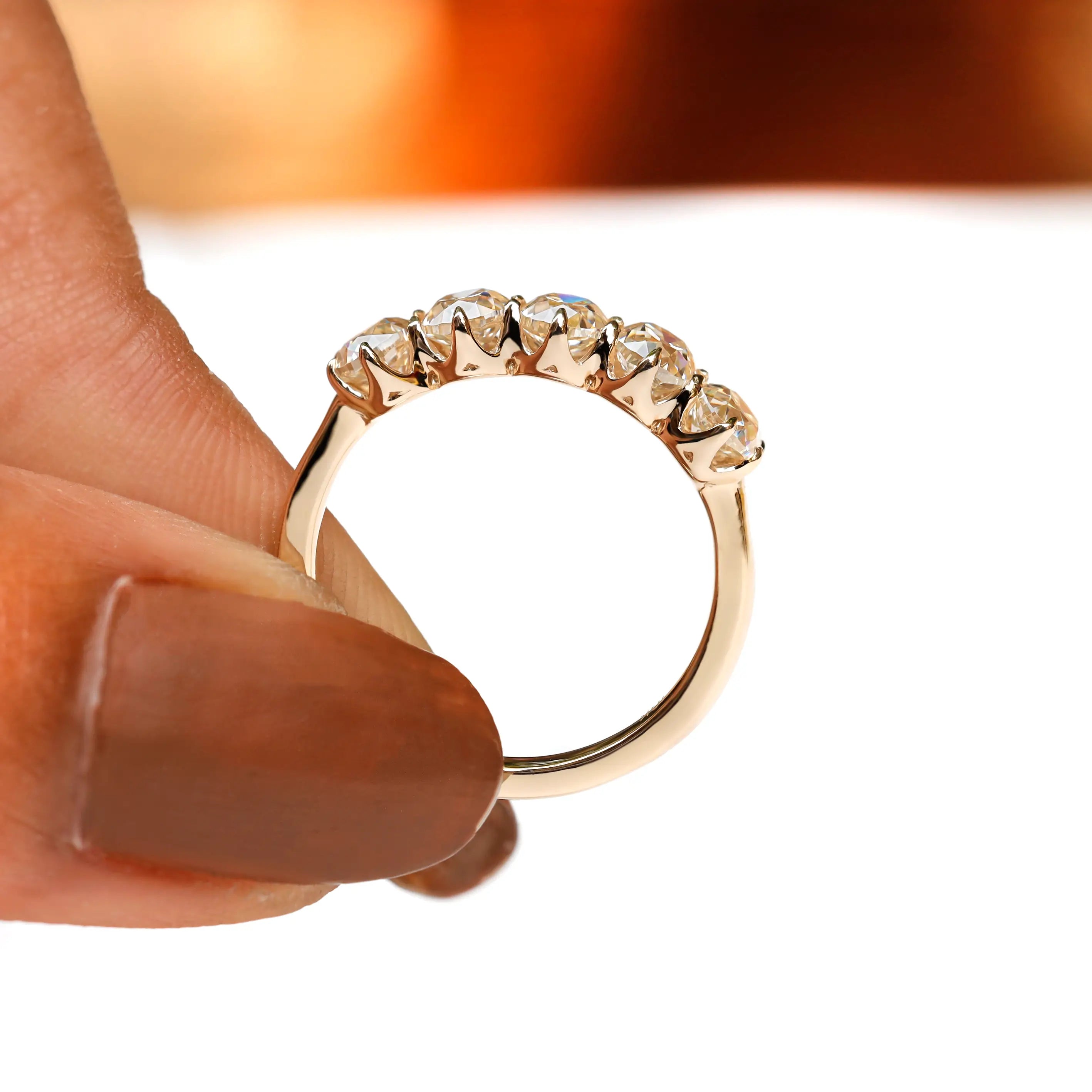 Profile close-up of five stone moissanite band held between fingers