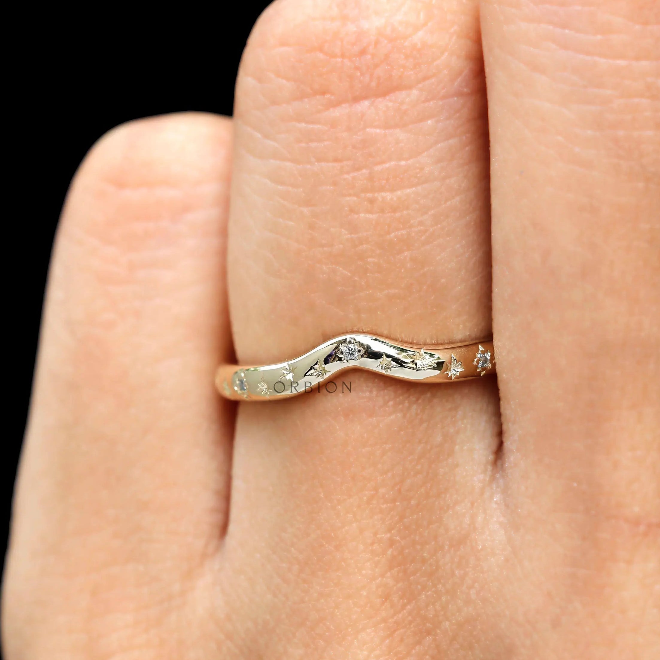 On-hand lifestyle image of starburst curved band styled as a stacking ring.