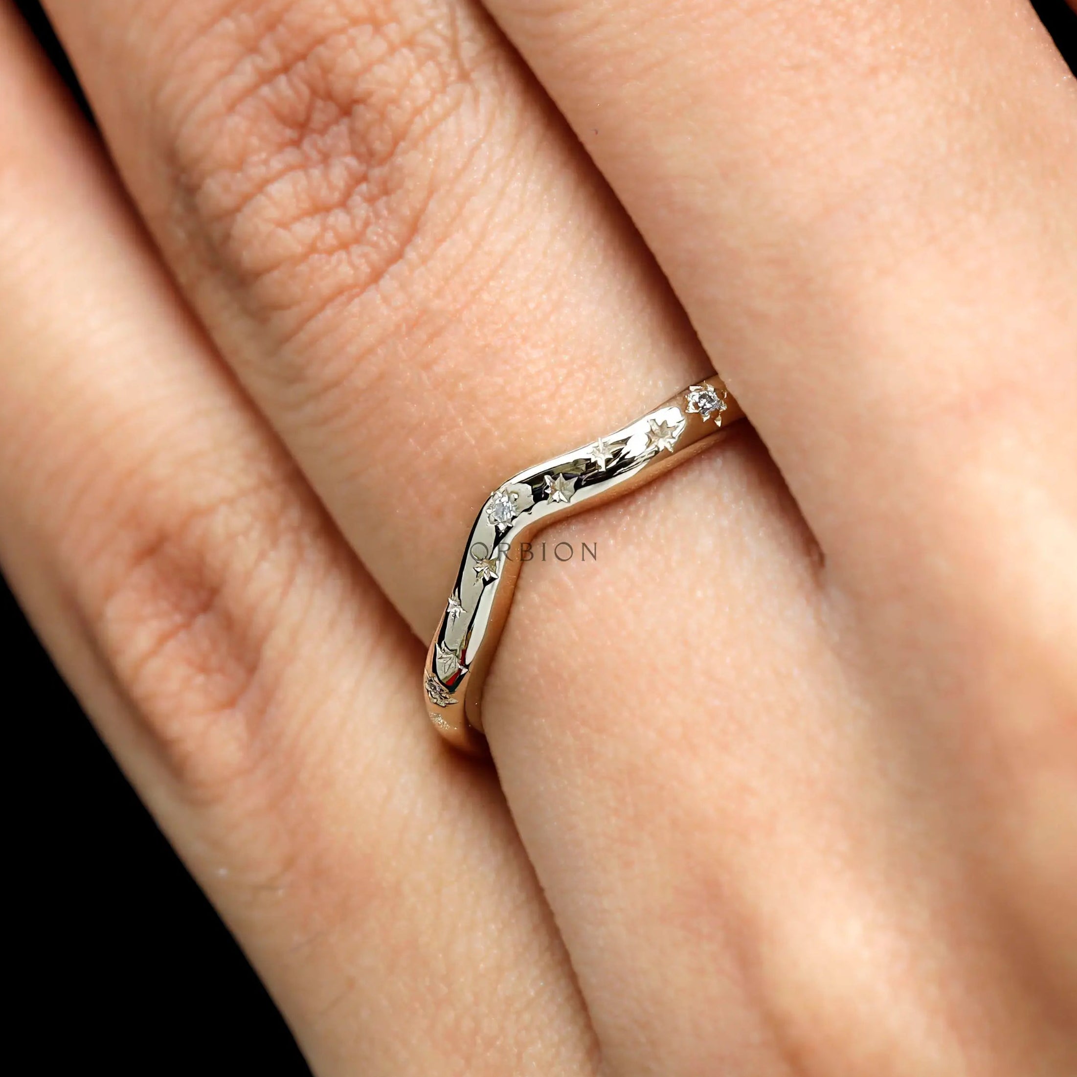 Close-up on finger of curved wedding band highlighting starburst sparkle.