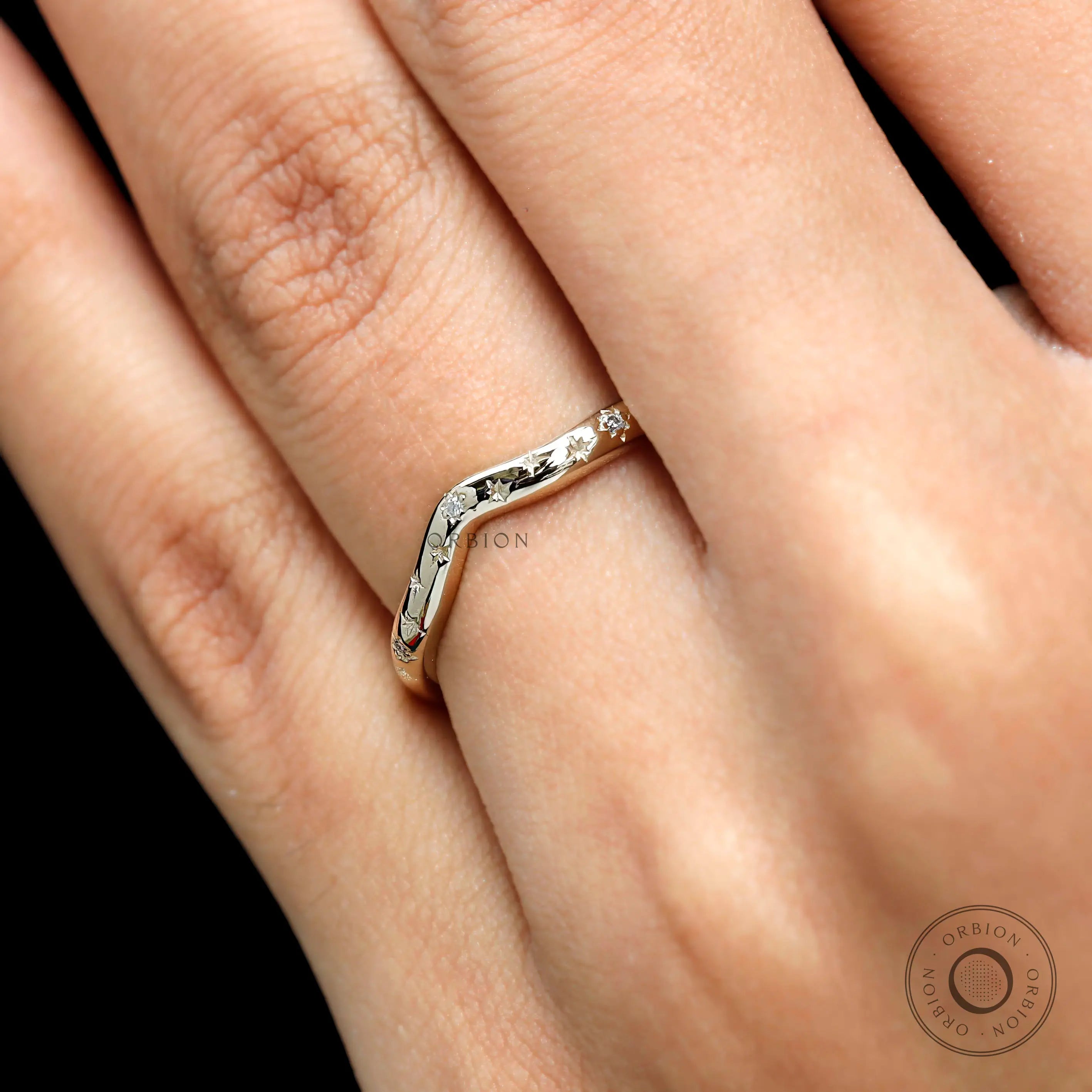 Close-up on finger of curved wedding band highlighting starburst sparkle.