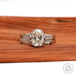 Elongated Cushion Moissanite ring set with brilliant side stones in 10K white gold, on a textured wooden surface