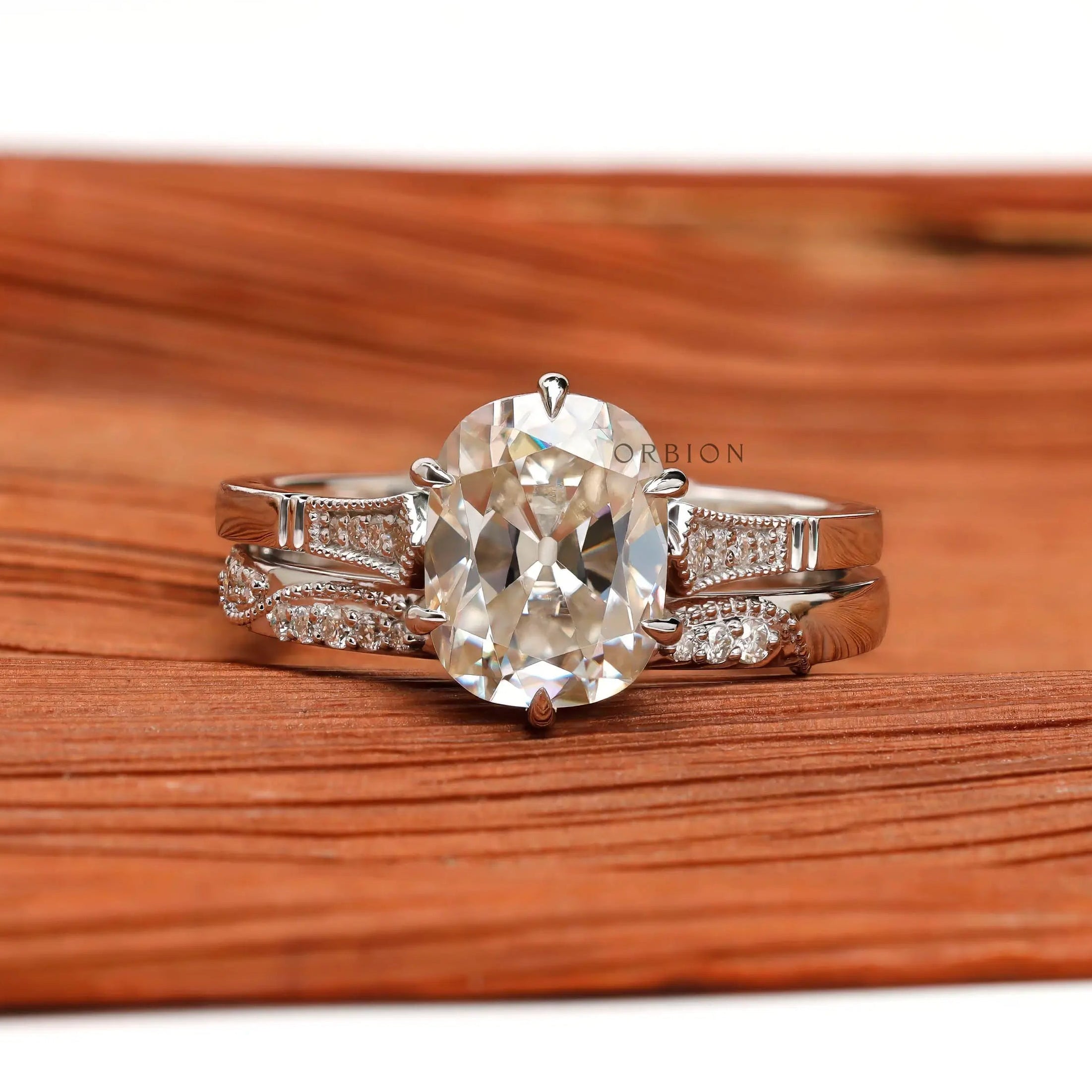 Elongated Cushion Moissanite ring set with brilliant side stones in 10K white gold, on a textured wooden surface