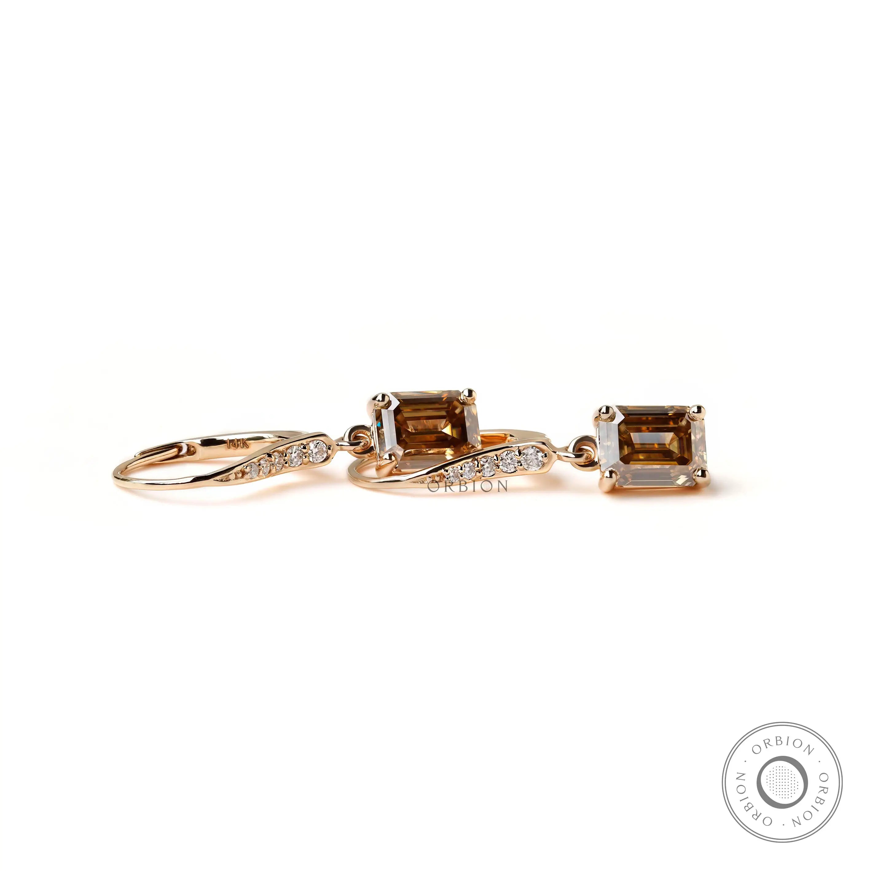 Yellow gold dangling earrings with step cut emerald champagne moissanite close up