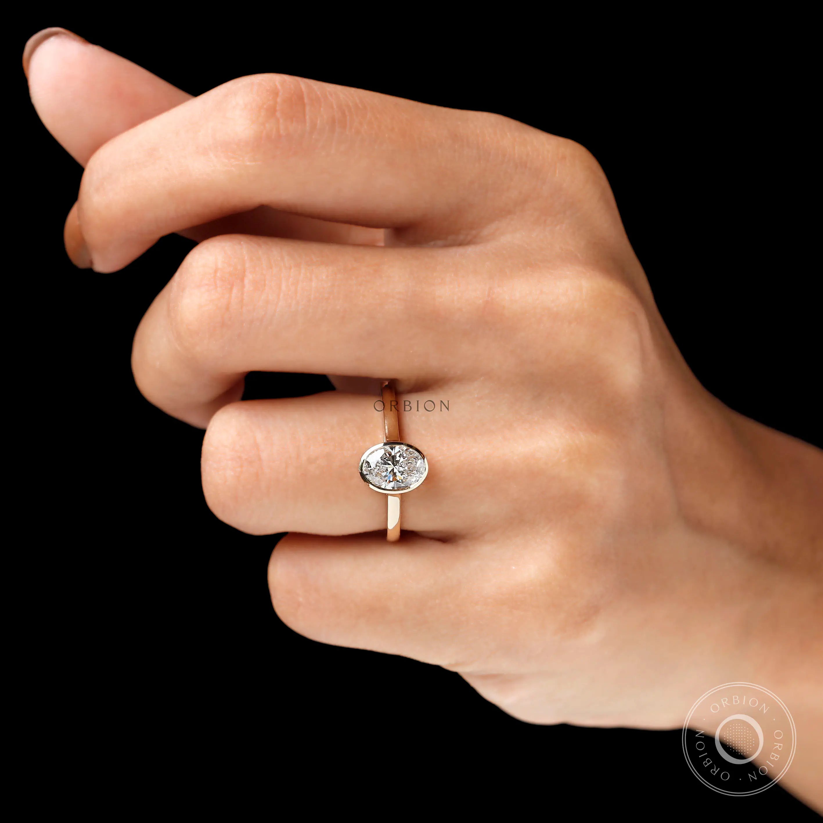 Oval bezel lab diamond ring worn on hand black background