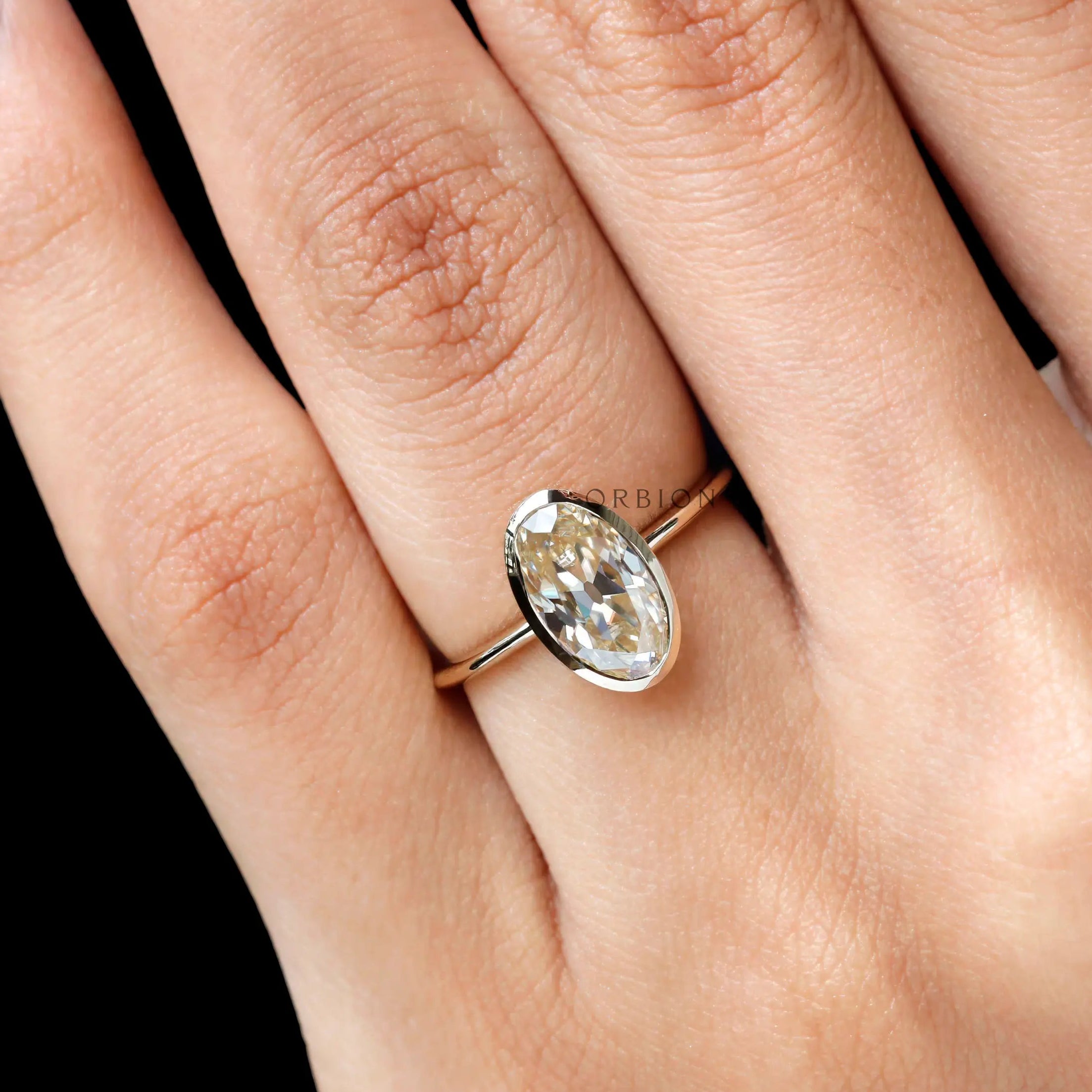 Angled closeup on hand oval champagne bezel ring in yellow gold
