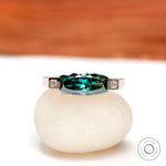 Front view of east west blue green ring with square bezel-set diamond accents in yellow gold.