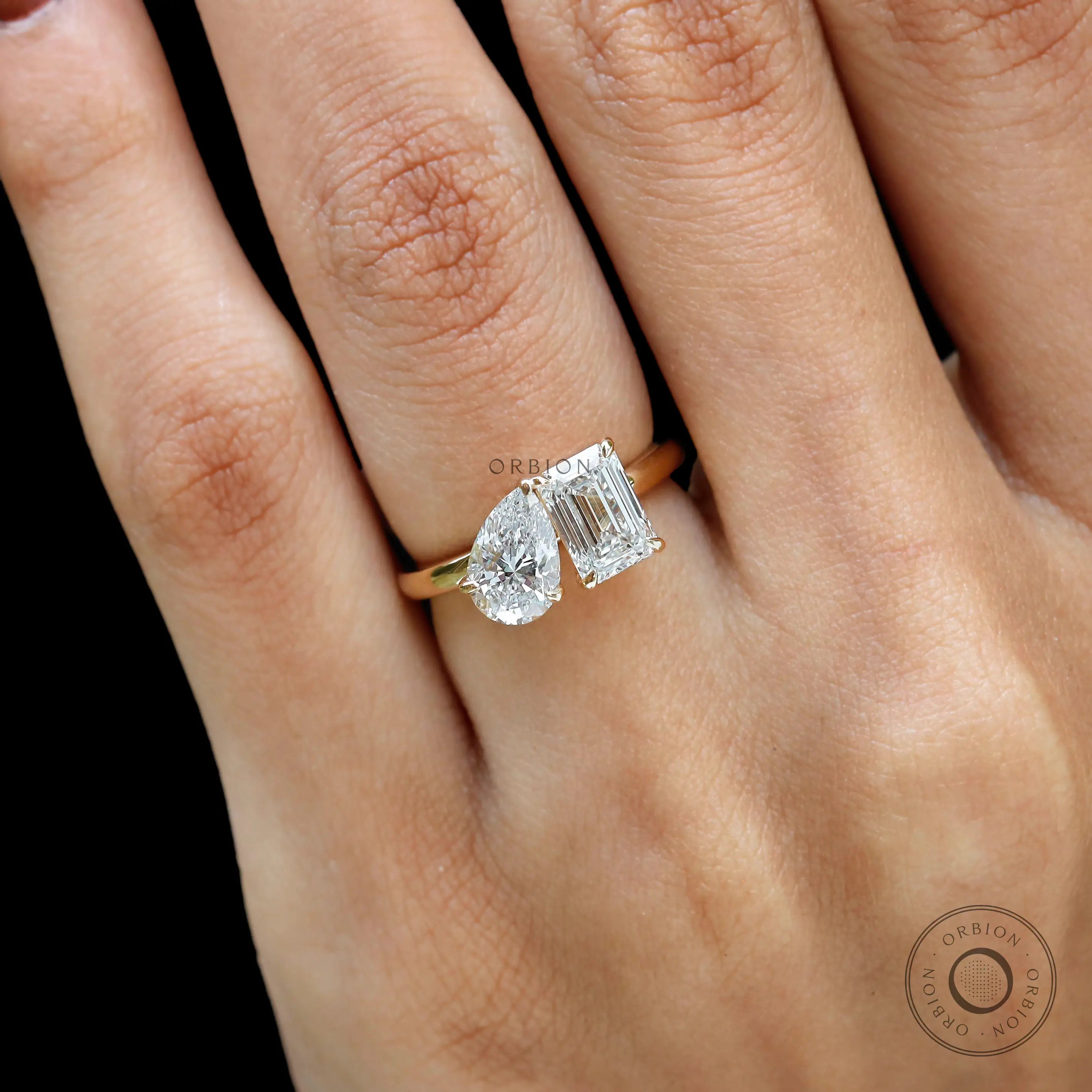 Closeup on hand showing contrast between pear and emerald lab diamonds.
