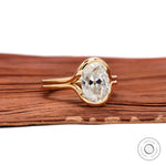 Angled view oval moissanite half bezel ring on wood backdrop