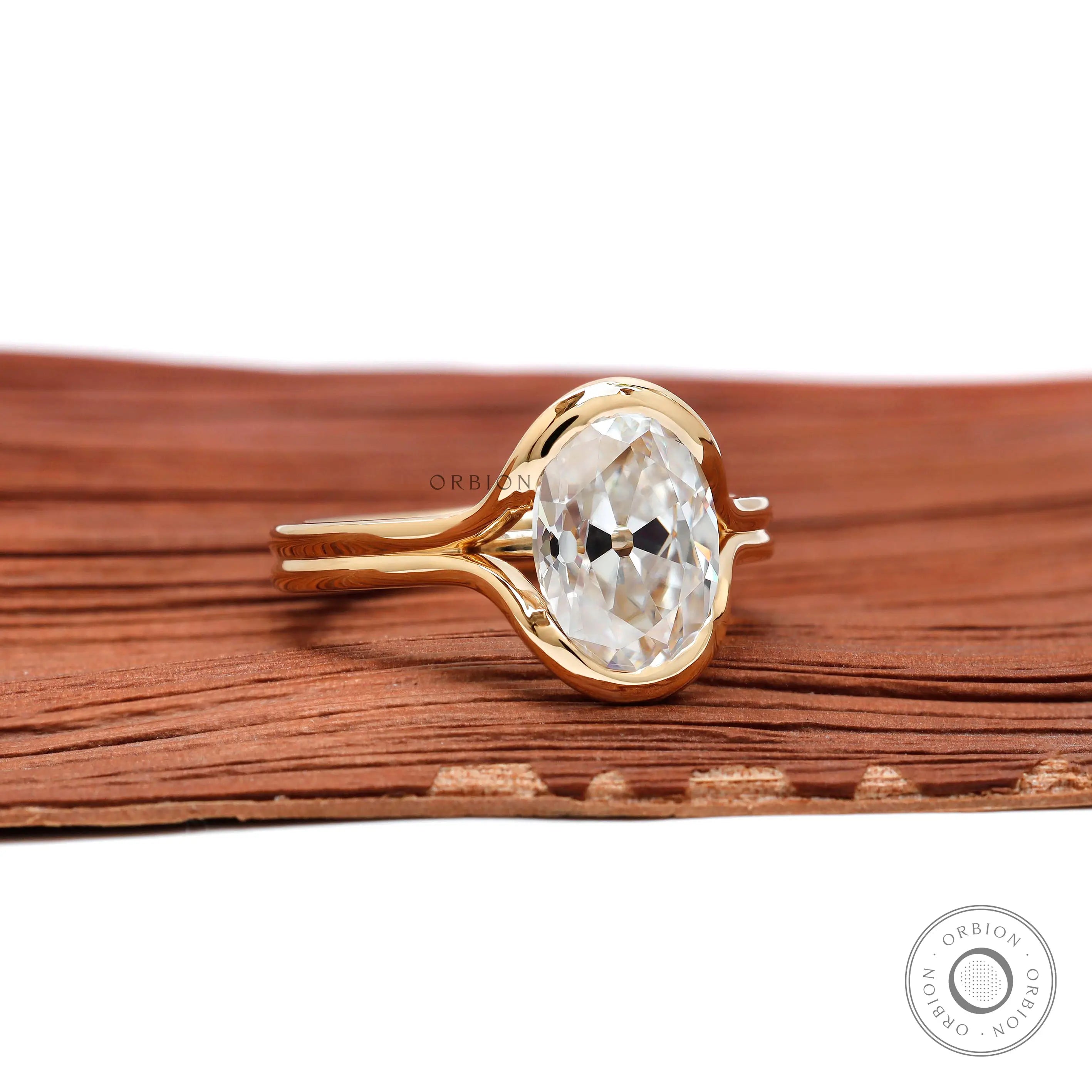 Angled view oval moissanite half bezel ring on wood backdrop