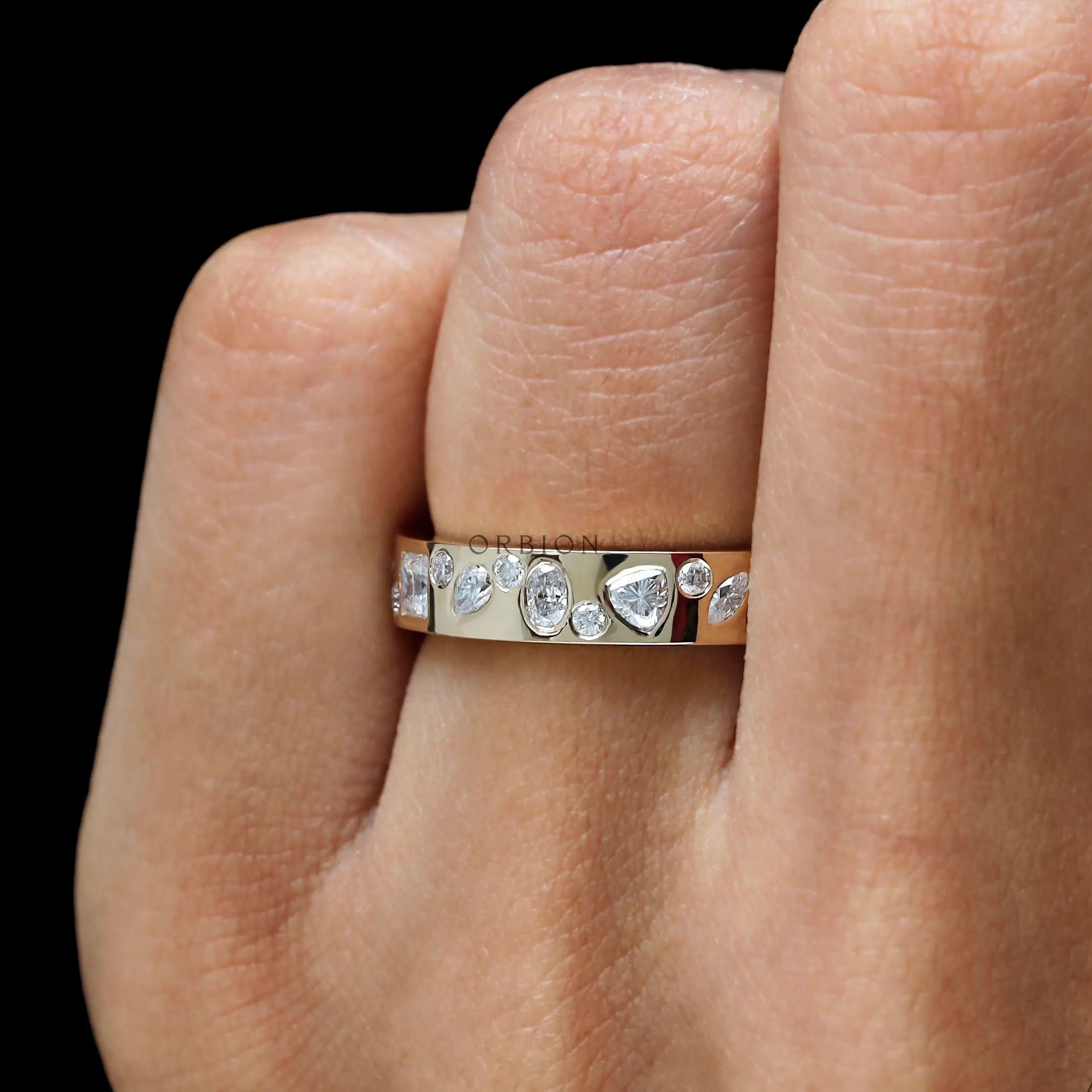 Close-up on finger showing mixed stones set in yellow gold band.