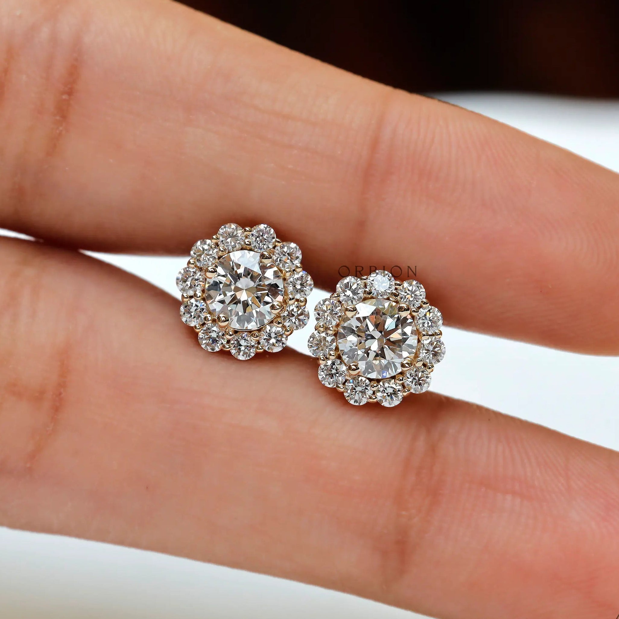 Lab diamond halo studs displayed on finger for size reference